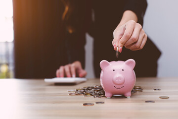 An Asian woman is putting coins into a piggy bank to practice saving discipline for future use, money saving concept.