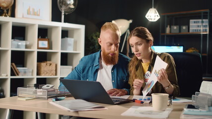 Young business couple showing documents in front of laptop screen in office