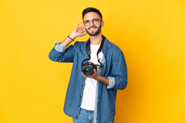 Young photographer girl isolated on yellow background having doubts