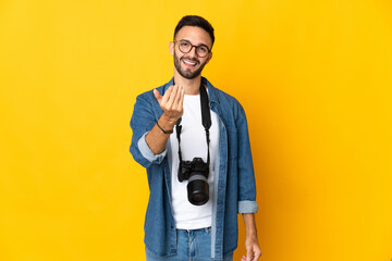 Young photographer girl isolated on yellow background inviting to come with hand. Happy that you came