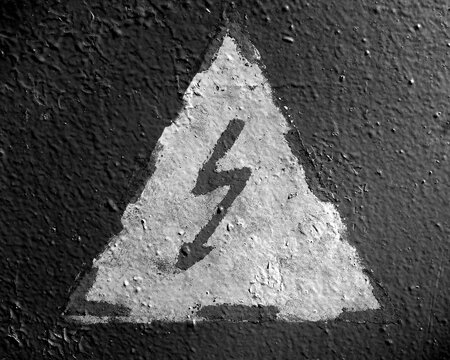 Hand painted electricity hazard sign on grungy surface in black and white