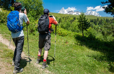 Fototapeta na wymiar Hikers on trail to Koruldi Lakes in Caucasus Mountains of Georgia near Mestia stop to take photos of Mt Ushba