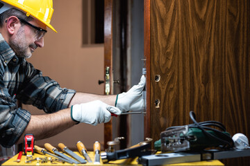 Close-up. Carpenter at work repairs and installs the new lock of a wooden door. Construction...