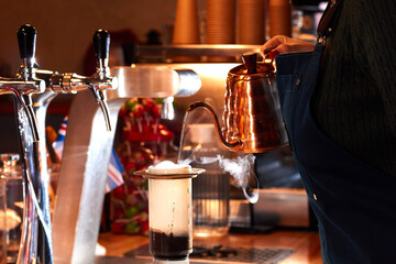 Hands of barista holding steel kettle and pours water into an aeropress. Professional barista pouring hot water in aeropress, alternative coffee brewing method.
