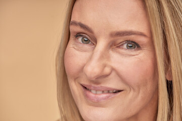 Perfection. Portrait of a charming happy middle aged caucasian woman with clean and soft skin smiling at camera while posing over beige background in studio