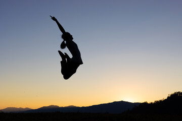 Silhouette of happy girl jumping playing on mountain at sunset