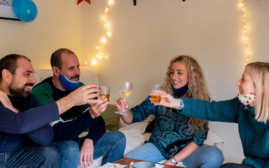 FRIENDS, TWO WOMEN AND TWO MEN TOASTING AT HOME WITH RED WINE, WHITE AND BEER, WITH LIGHTS ON THE WALL AND MASKS ON THE NECK