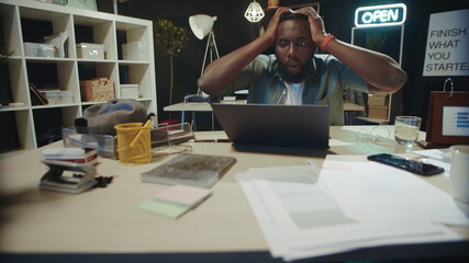 Frustrated african american guy checking project result online in dark office.