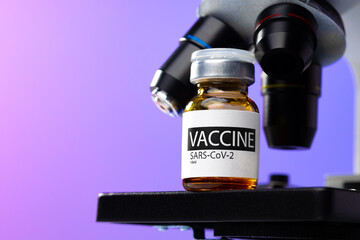 Vial of Covid-19 vaccine next to a microscope
