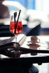 A table in a cafe. A glass with a red cocktail and a cup of coffee on the table.