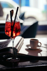 A table in a cafe. A glass with a red cocktail and a cup of coffee on the table.