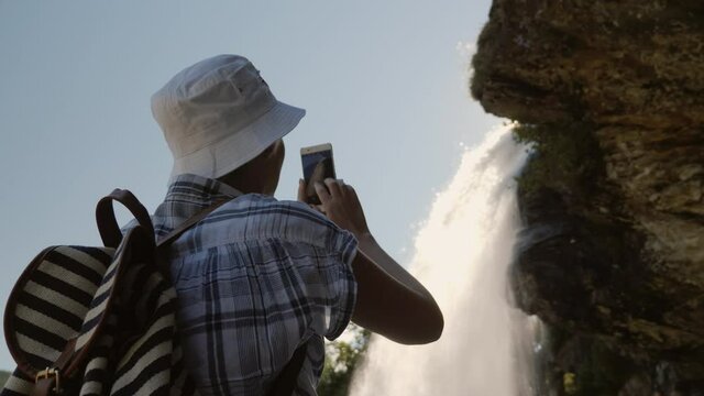 A silhouette of a woman taking pictures of a beautiful waterfall in Norway