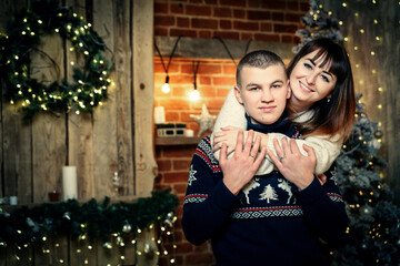 Beautiful girl with dark hair hugs her boyfriend from behind on the background of Christmas decorations