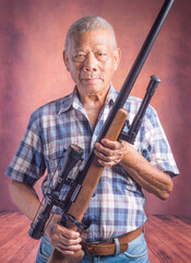 Portrait of an elderly Asian man holding a sport air rifle with a telescopic while standing with a...