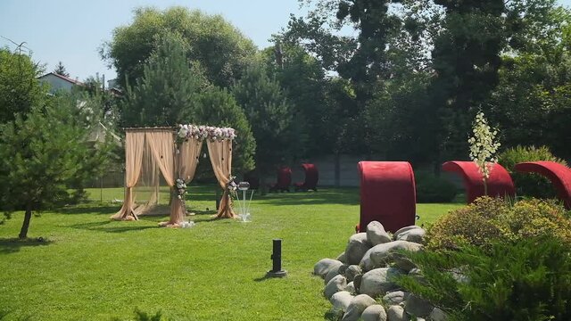Wedding decor. Beautiful wedding arch with fresh flowers and red armchairs in the garden on a summer sunny beautiful wedding day