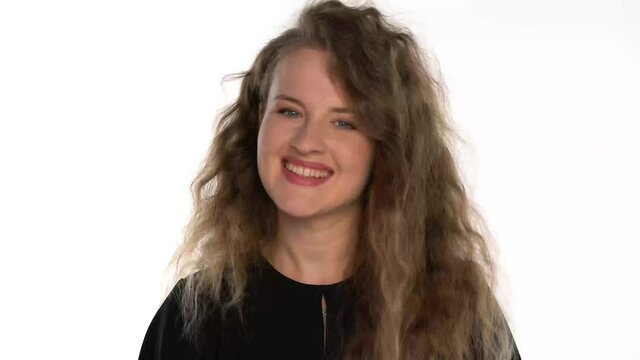 a young woman with long curly blonde hair turns to the camera in surprise and smiles on a white background
