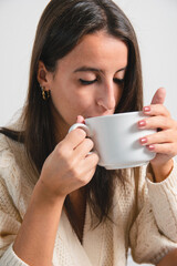 Comfortable woman at home drinking a cup of coffee or tea with warm woolen clothes. Concept being at home