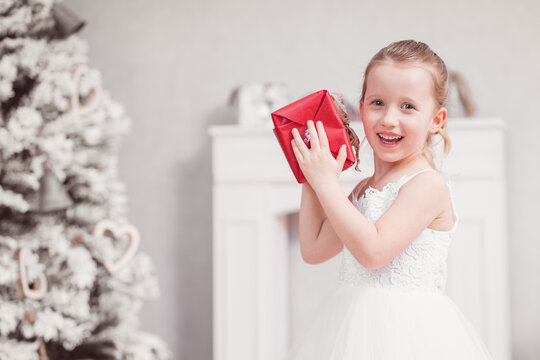 Weihnachten Xmas Portrait Mädchen schaut uin Kamera weißes Kleid mit rotem Geschenk vor Kamin und Tannenbaum Var. 3
