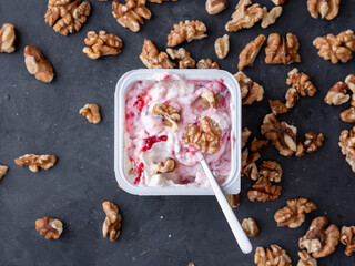 White yogurt in plastic square cup with marmalade and spoon in with walnuts on gray background. Flat view.