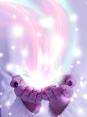 The stream of energy emanating from a close-up of female hands on a light abstract background. Neon glow, bokeh, magic particles