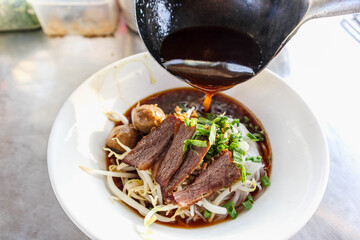 The broth is being poured into a dish with noodles, beef, and vegetables in preparation for cooking and serving the customers. Concept: food arrangement and decoration.