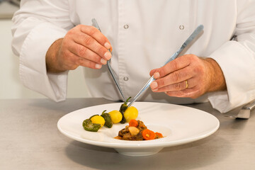 view of a male chef decorating a beef stew plate alternating potatoes and green pepper with pliers