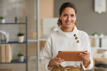 Waist up portrait of elegant modern businesswoman holding tablet and looking at camera with...