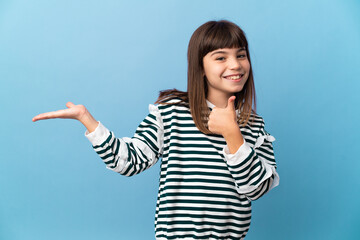 Little girl over isolated background holding copyspace imaginary on the palm to insert an ad and with thumbs up