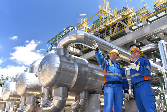 teamwork: group of industrial workers in a refinery - oil processing equipment and machinery