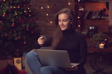 Beautiful woman using laptop computer, doing Christmas online shopping at home, paying with credit card.