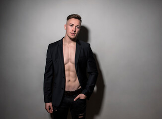 Fototapeta premium Handsome young bodybuilder with fit and athletic build wearing blazer on grey background