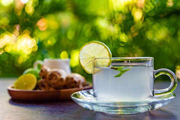 side view, ginger tea with a slice of lime and mint leaves, a wooden plate with ginger root and whole lime in the background