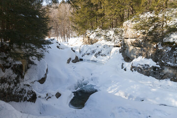 Fototapeta na wymiar Warren falls - frozen creek under ice and snow with rocky shores. Sunny winter day