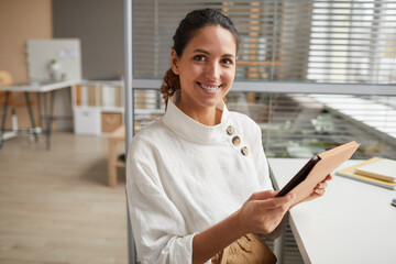 Waist up portrait of smiling successful businesswoman using digital tablet and looking at camera...