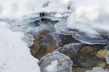 Warren falls - frozen creek under ice and snow with rocky shores. Sunny winter day