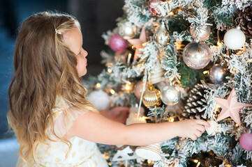 Portrait of a cute blonde little girl looking at decorations on the Christmas tree.