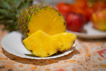 Pineapple fruit on white plate and red apples in the background