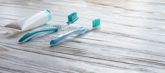 Two toothbrushes and a tube of toothpaste lie on the white surface of the table in the vanized room. Accessories for brushing blue teeth.