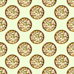 Top view flat lay pistachio nuts in a round wooden bowl repeat seamless pattern on light green background.