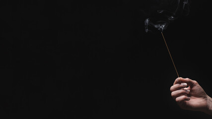 hand holding an incense stick on black background