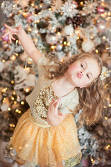 Portrait of a cute little girl with a crown on her head making lips with a bow near the Christmas tree.