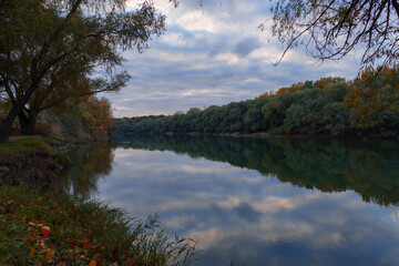 autumn landscape, beautiful sunset and bright colorful forest in the evening, trees near river and blue sky