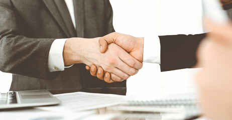 Unknown diverse business people are shaking hands finishing up meeting at the desk in office, close-up. Handshake concept