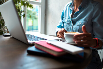 Cropped shot woman is using a white blank screen computer laptop at the wooden table.Cup of coffee on table with woman sitting by working on laptop. Woman using laptop computer at cafe with coffee cup