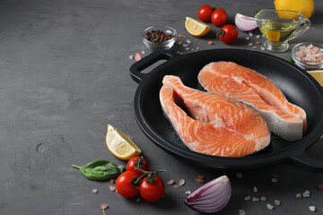Fresh raw salmon steaks in a grill pan and ingredients on a dark background. Copy space
