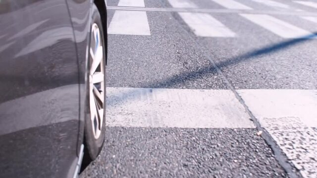 The car stop before a zebra crossing is a type of un-signallized pedestrian crossing. The movement of car wheel on an asphalt road in the city. Vehicle maneuver at an intersection during rush hour. 