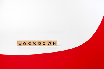 Wooden letters on a white and red background forming the word “lockdown”. Second wave during Coronavirus pandemic concept..
