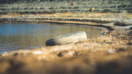 Old dirty car tire on the shore of a reservoir.
