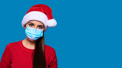 Fototapeta na wymiar Caucasian woman in protective medical mask and Santa hat on blue isolated background. Christmas on quarantine.