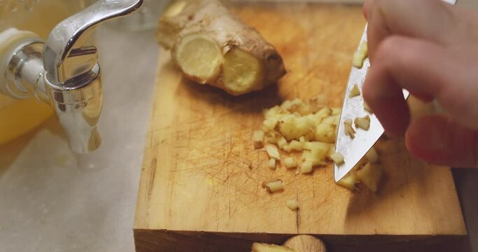 Slicing fresh ginger root on a wood cutting board. Raw spicy root used for healthy beverage kombucha, fresh pressed juices, and fresh home cooked meals